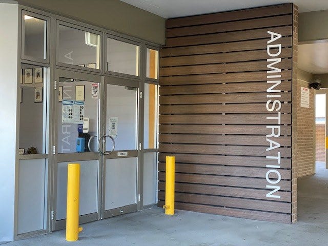 Front door of administration block. 2 yellow pillars and wooden wall with administration on it