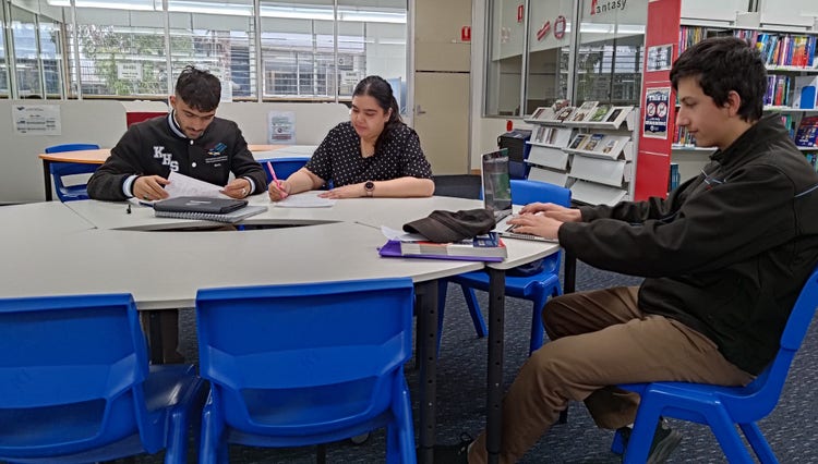 Two students and a teacher working at a desk in the library.