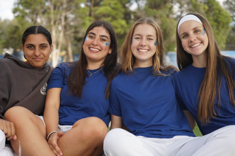 4 female students wearing blue shirts, smiling with face paint